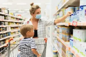 New normal in shopping. Young mother wearing prevention mask and her little son in a supermarket during virus pandemic.
