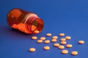 Orange pill bottle, with orange pills spilling out on a blue background