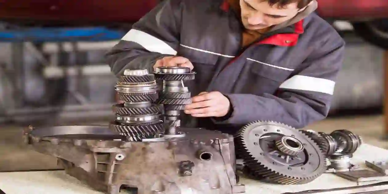 Auto mechanic in workshow working on transmission on a wooden tabke