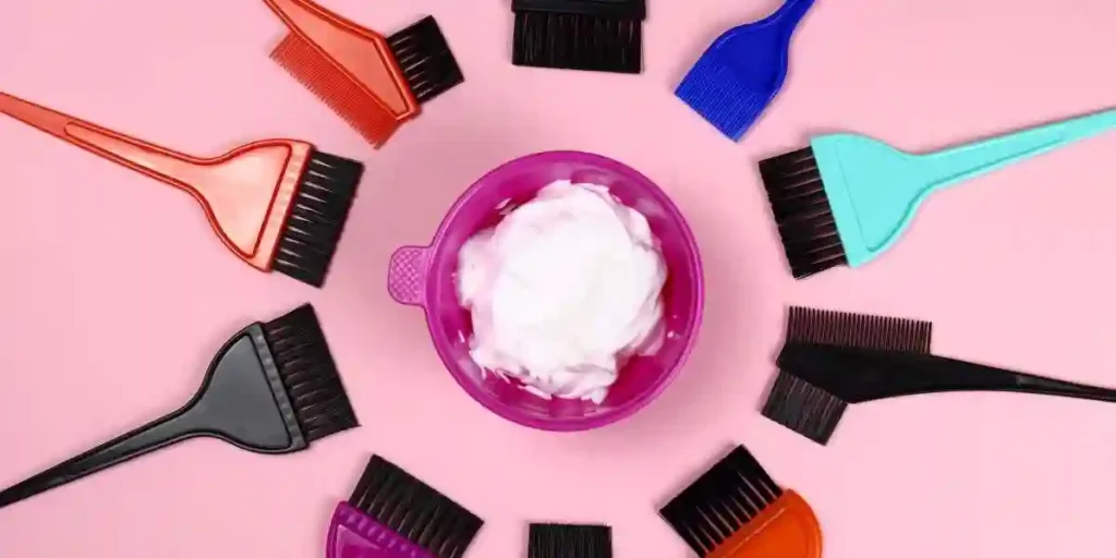 Hair coloring tools - plastic bowl with hair dye and brushes on pink background used in hair dye lawsuits